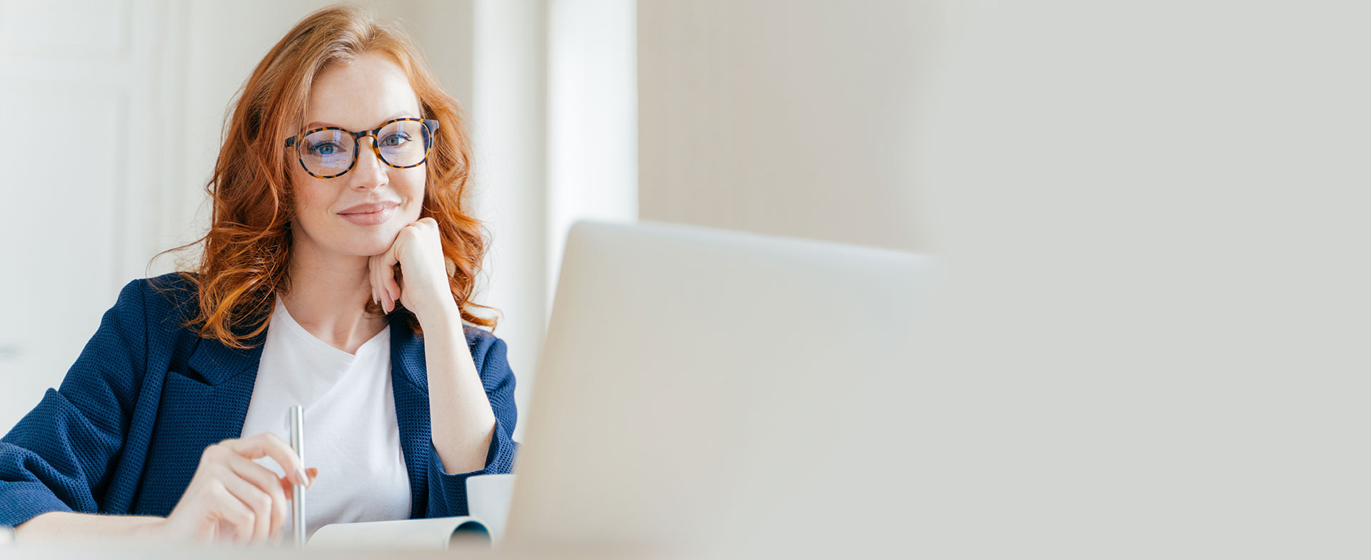 A woman reading a computer screen with pen in hand